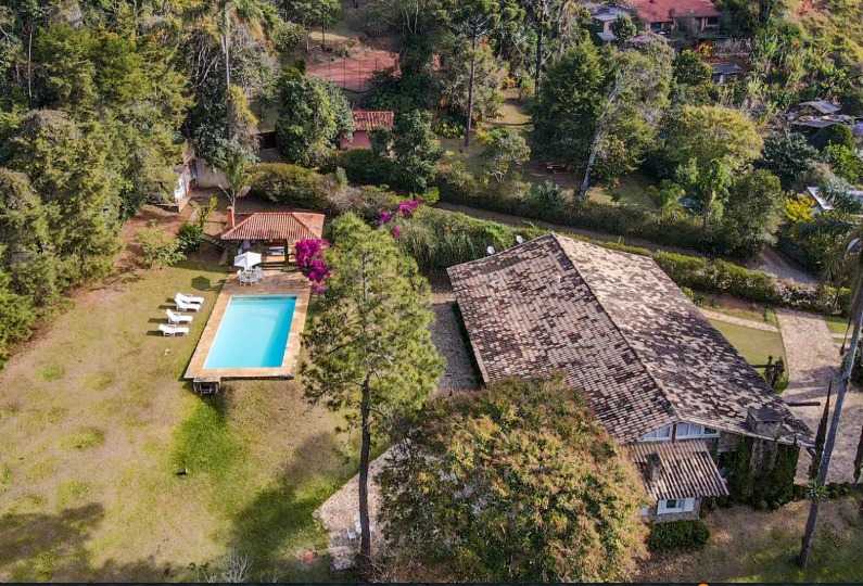 Vista aérea da Pousada FAVO: casa de telhado grande, piscina retangular, quiosque e gramado cercados de mata