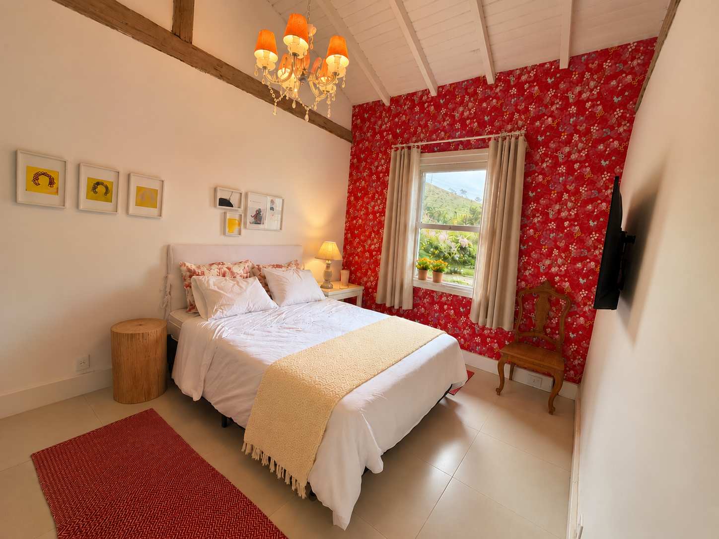 Suíte 04: cama de casal com manta amarela, parede de papel floral vermelho, janela para as montanhas, lustre de cúpulas laranja e viga de madeira